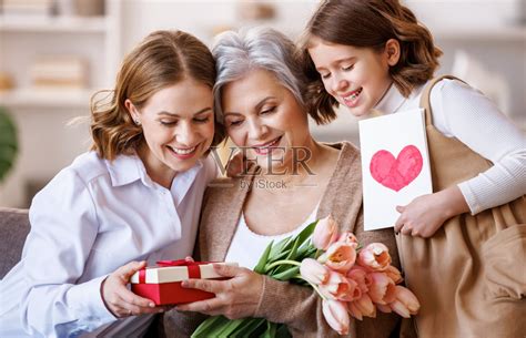 国际妇女节快乐。女儿和外孙女微笑着给祖母送花和礼物，在家庆祝春节母亲节照片摄影图片_ID:417966763-Veer图库