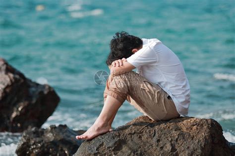 压抑着痛苦的亚洲男人坐在海边岩石的高清图片下载-正版图片505305254-摄图网
