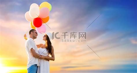 爱情、夏天、约会和生日概念-幸福的情侣戴着太阳镜和气球拥抱在夕阳的天空背景。高清摄影大图-千库网