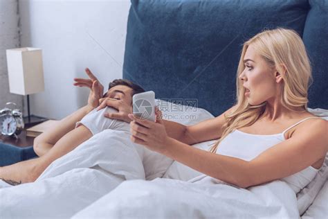 愤怒的老婆用智能手机向躺在床上的困惑丈夫展示了不信任概念高清图片下载-正版图片503370269-摄图网