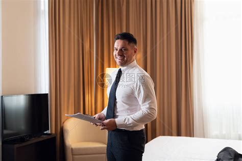 一位年轻快乐的旅行者商人穿着一件白衬衫和一条领带站在旅馆房间里高清图片下载-正版图片506700179-摄图网