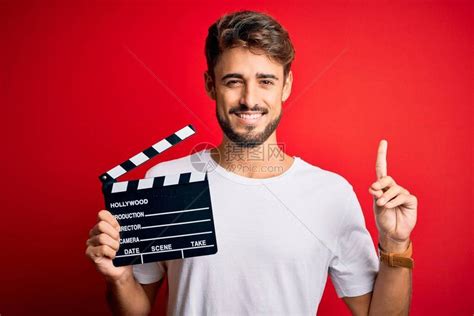 留着胡须的年轻导演在孤立的红色背景上用隔板制作电影高清图片下载-正版图片504204037-摄图网