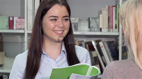 可爱的年轻女子笑着和她在大学图书馆的朋友交谈快乐的女学生在图书馆准备大学考试女朋友在书店聊高清图片下载-正版图片505821342-摄图网