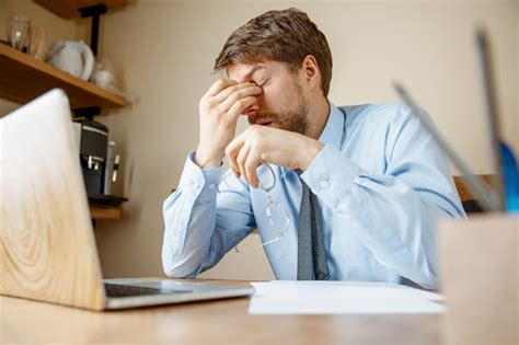 精疲力竭的商人坐在笔记本电脑旁，一边举着眼镜，一边触摸着眼睛 高清摄影大图-千库网