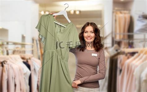 销售、购物和商业概念-快乐的女店员或女售货员在服装店背景的衣架上穿裙子。高清摄影大图-千库网