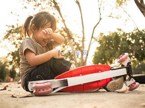 可爱的亚洲小女孩从滑板车上摔下来后坐在地上。高清摄影大图-千库网
