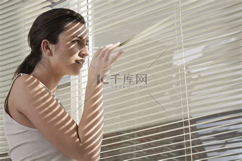 年轻女子透过家里的百叶窗凝视高清摄影大图-千库网