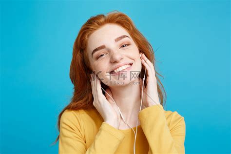 生活方式概念 — 欢快快乐的姜红头发女孩的肖像喜欢戴着耳机听音乐，对着镜头欢快地微笑。高清摄影大图-千库网