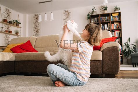 一个十几岁的女孩和她心爱的毛茸茸的白色小猫玩耍。孩子亲吻猫。爱护宠物。公寓里宠物的生活图片-商业图片-正版原创图片下载购买-VEER图片库