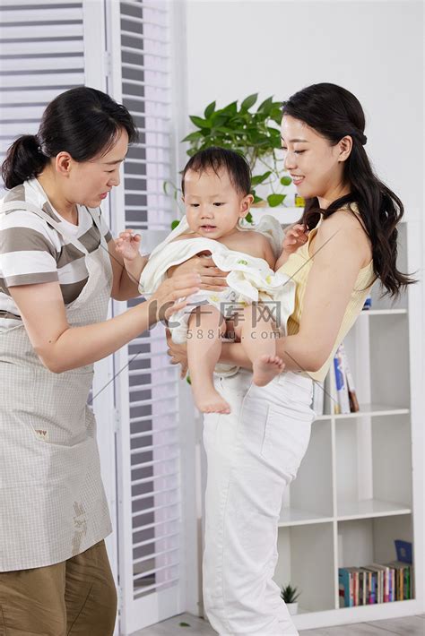 月嫂和年轻妈妈一起照顾洗澡后的宝宝高清摄影大图-千库网