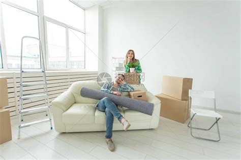 满意的快乐年轻夫妇强壮的男人和漂亮的女人手里拿着他们的东西坐在新公寓的客厅高清图片下载-正版图片506205901-摄图网