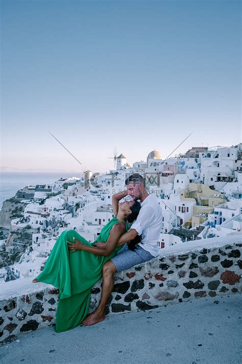 希腊圣托里尼岛，年轻夫妇在圣托里尼岛豪华度假，在日出期间在蓝色圆顶教堂和希腊伊亚圣托里尼粉刷成白色的村庄旁观看日出，男女在希腊度假高清摄影大图-千库网