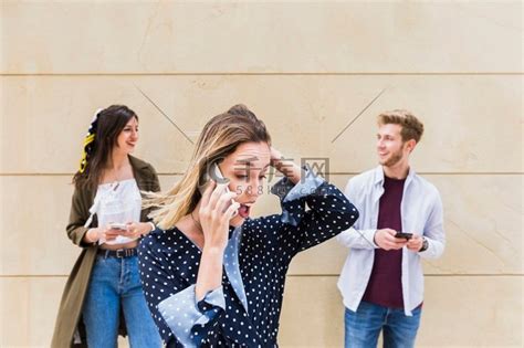 惊讶的年轻女人站在朋友面前用手机看着对方高清摄影大图-千库网