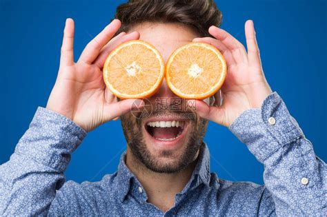 年轻人用蓝色背景上的橘子遮住眼睛高清图片下载-正版图片502715994-摄图网