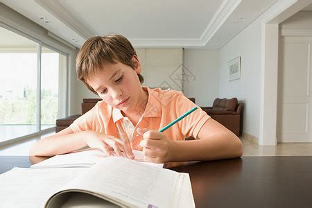 特写的可爱的小学生男孩做家庭作业写笔记本与钢笔坐在书桌上