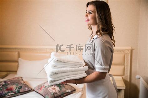 微笑的年轻女服务员拿着一叠干净的毛巾站在卧室酒店附近高清摄影大图-千库网