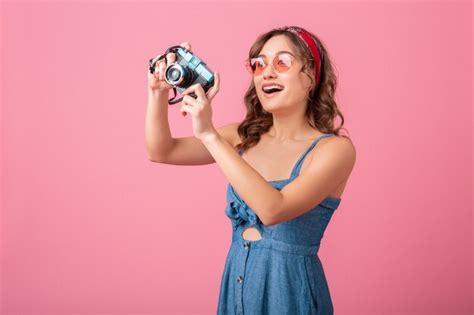 분홍색 배경에 고립 된 데님 드레스와 선글라스를 착용하는 빈티지 카메라에 매력적인 웃는 여자 복용 사진 | 무료 사진