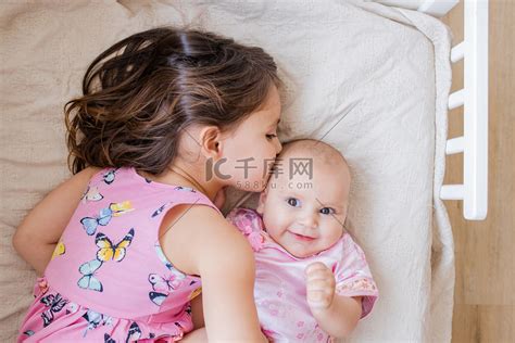 小女孩在床上深情地拥抱和亲吻她的小妹妹高清摄影大图-千库网