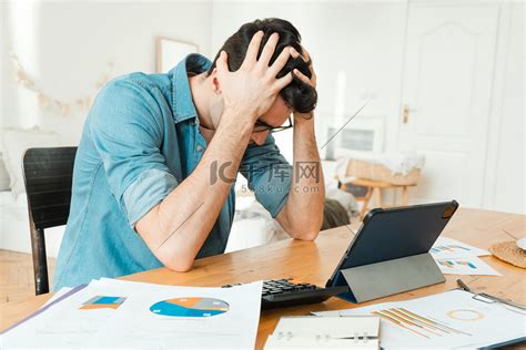 忧心忡忡的男人坐在家里的桌旁，抱着头，担心他的账单。高清摄影大图-千库网