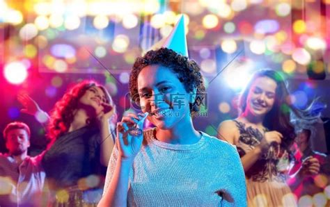 生日、庆典和夜生活概念-快乐微笑的年轻非洲裔美国妇女在派对帽与鼓风机在紫外线霓虹灯在夜总会背景。高清摄影大图-千库网