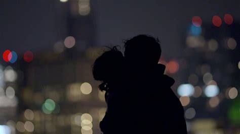 当烟花在远处绽放时，一对年轻的情侣在城市的天际线上亲吻视频素材_ID:VCG42645949231-VCG.COM