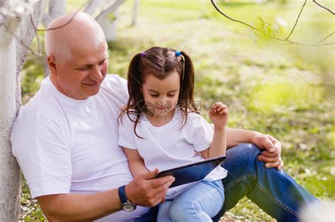 祖父抱着小孙女坐在春天盛开的公园绿草上的数高清图片下载-正版图片505461023-摄图网
