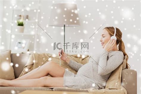 怀孕、孕产、技术、人和期望概念-快乐的孕妇带着智能手机和耳机在雪地上在家里听音乐。高清摄影大图-千库网
