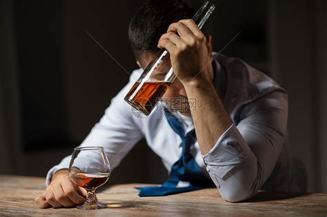 酒精中,酒精成瘾人的男酒精与瓶子喝白兰地桌子上晚上醉汉晚上桌子上喝酒高清图片下载-正版图片300156128-摄图网