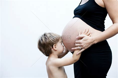 怀孕和人的概念-快乐微笑孕妇与婴儿紧身衣裤在家里的沙发上。美女吊带睡衣高清摄影大图-千库网