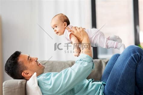 家庭、父亲身份、财务和父母身份概念-快乐微笑的年轻父亲和小宝宝在家里玩存钱罐。高清摄影大图-千库网