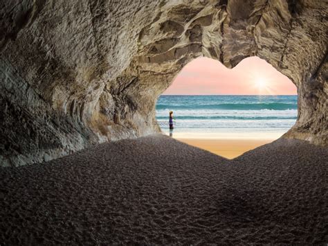 自然风景素材设计夕阳西下海边的山洞在阳光下形成一个心形影子一个人在岸边享受着自然的馈赠