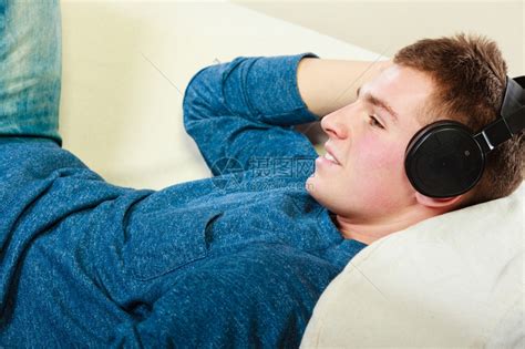 英俊的年轻人带着耳机躺在沙发上家里听音乐高清图片下载-正版图片304046461-摄图网