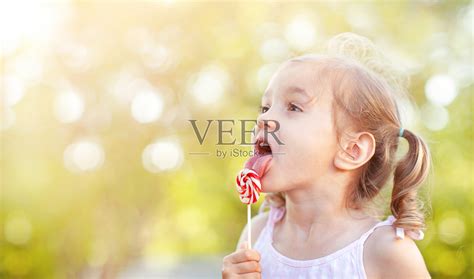 一个小女孩在舔棒棒糖照片摄影图片_ID:420669221-Veer图库