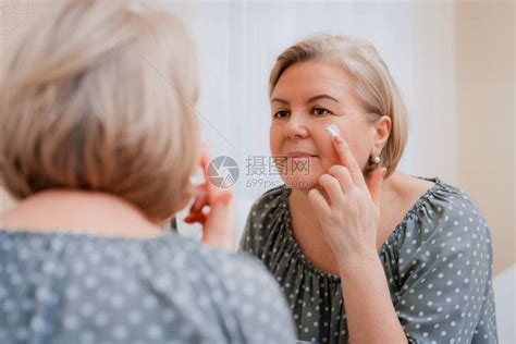 镜子前快乐健康的成熟女在脸上涂抹抗衰老保湿化妆霜高清图片下载-正版图片506440206-摄图网