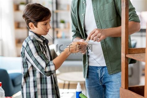 家庭、医学和健康概念-父亲在家里用医疗贴片治疗儿子受伤的手指。高清摄影大图-千库网