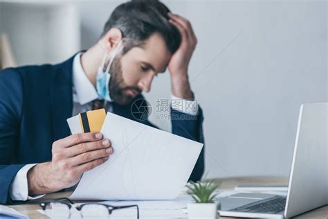 沮丧的商人在低头闭眼坐在工作场所时拿着纸和信用卡高清图片下载-正版图片503757821-摄图网