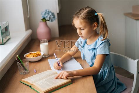 从高角度看，漂亮的小学生女孩用钢笔在笔记本上写书。照片摄影图片_ID:415085198-Veer图库