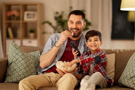 家庭、父亲身份和人的概念-快乐的父子在家里看电视吃爆米花。全家福人物特写高清摄影大图-千库网