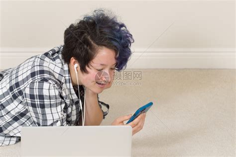 微笑的少女看着手机电脑放在前台躺家里听音乐高清图片下载-正版图片304109494-摄图网