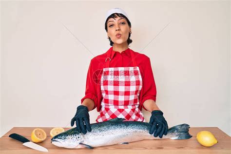 美丽的黑发女鱼贩子煮新鲜生鲑鱼看着摄影机拍出一个可爱感的高清图片下载-正版图片506733676-摄图网
