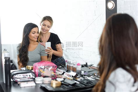 美丽的年轻女士和微笑的化妆师在智能手机上一起拍自的高清图片下载-正版图片503381732-摄图网