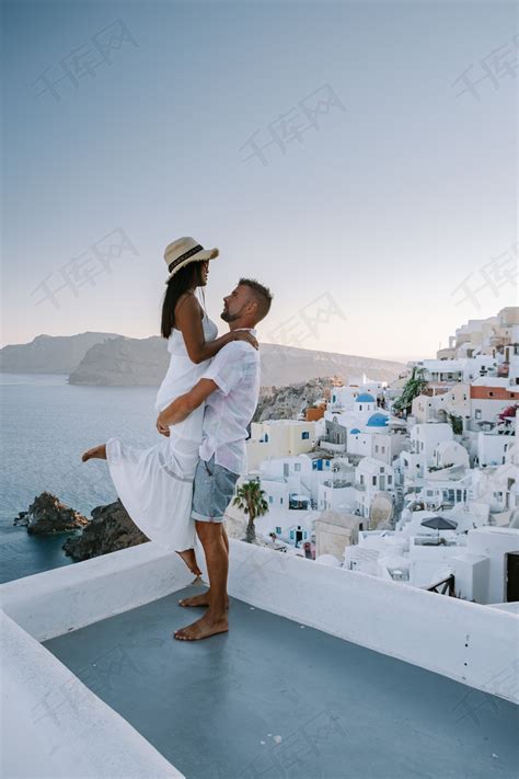 希腊圣托里尼，年轻夫妇在圣托里尼岛享受豪华假期，在蓝色圆顶教堂和粉刷成白色的希腊伊亚圣托里尼村观看日出高清摄影大图-千库网