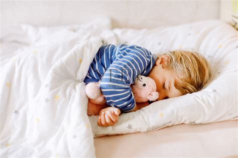 可爱的小女孩和心爱的毛绒玩具喇嘛一起睡在床上。可爱的宝贝孩子做梦，健康的孩子白天睡觉。照片摄影图片_ID:413270876-Veer图库