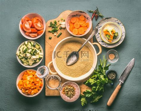 蒸粗麦粉和素食烹饪配料放在带勺子、灰色背景、顶视图的切板上的碗中高清摄影大图-千库网