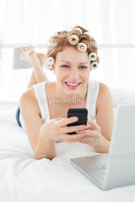Portrait of a smiling young woman in hair curlers text messaging by ...